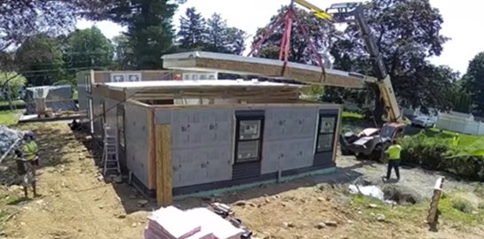 A crane setting a factory-built roof panel during assembly